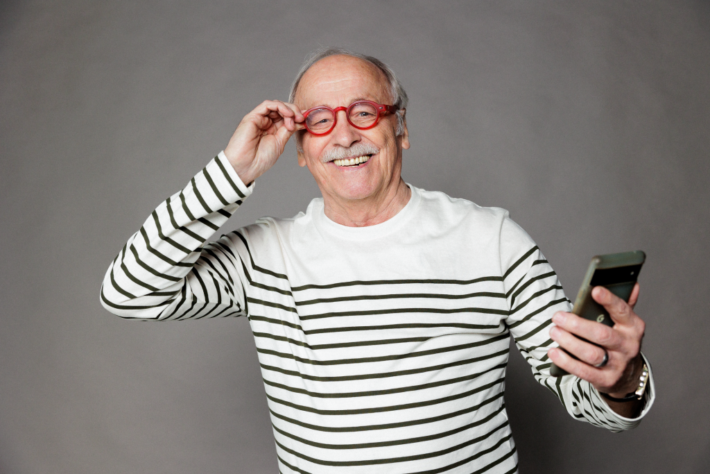 senior souriant avec des lunettes rouges et un téléphone à la main